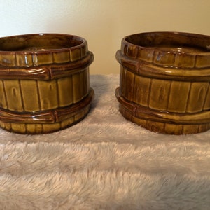 May include: Two brown ceramic planters with a bamboo design. The planters are round and have a wide opening.