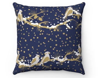 May include: A square cushion featuring a navy blue backdrop with a repeating pattern of gold branches, white snow, and gold birds. The birds are perched on the branches, and the snow dots the background.