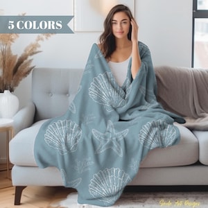 May include: A soft blue fleece throw blanket with a white seashell and starfish pattern. The blanket is draped over a light blue sofa.