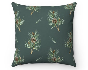 May include: Square throw pillow with a dark teal background featuring a repeating pattern of watercolor pine branches and pinecones. The branches have green needles and brown cones, creating a nature-inspired design.