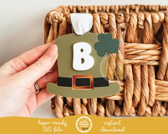 May include: A green leprechaun hat with a gold buckle and a shamrock on top. The hat is decorated with a white letter "B".