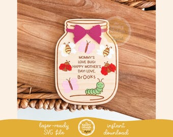 May include: A wooden craft project shaped like a mason jar with a pink bow and a message that reads "Mommy's Love Bug! Happy Mother's Day! Love, Brooks". The jar is decorated with butterflies, ladybugs, and bees.
