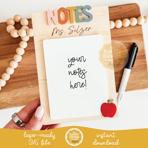 May include: A wooden clipboard with the word "NOTES" in colorful letters. It has a white notepad with the text "your notes here!" and a red apple accent. A black marker and a wooden bead garland are also visible.