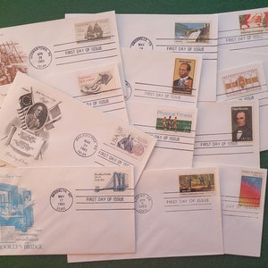May include: A collection of vintage first day of issue envelopes featuring various stamps, including a stamp of the Brooklyn Bridge, a stamp of a physical fitness scene, and a stamp of a historical figure. The envelopes are in various colors, including white, cream, and light blue.