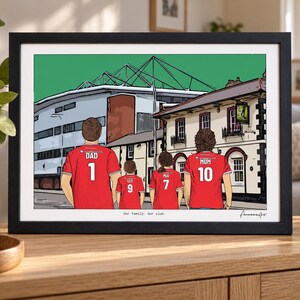 Pu&ograve; includere: Un'illustrazione incorniciata di quattro persone che indossano maglie da calcio rosse con numeri e nomi sul retro, davanti a uno stadio e un edificio. Il testo "Our family. Our club." &egrave; stampato in fondo all'opera.