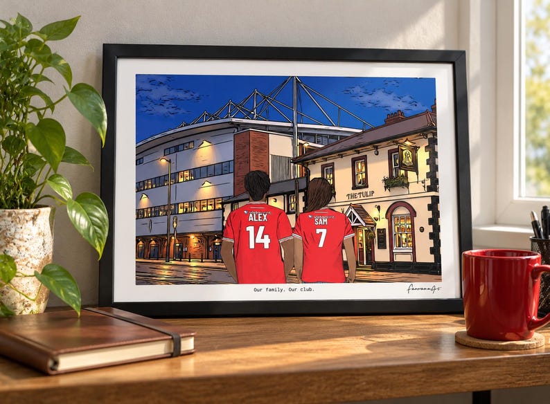 Pu&ograve; includere: Un'illustrazione incorniciata di due persone che indossano maglie da calcio rosse con i nomi ALEX 14 e SAM 7 sul retro, davanti a uno stadio e a un pub chiamato THE TULIP. La stampa include il testo Our family. Our club. in basso.