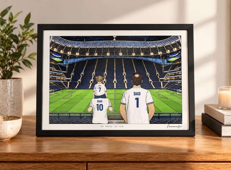 Puede incluir: Una ilustraci&oacute;n enmarcada de una familia de tres personas dentro de un gran estadio de f&uacute;tbol. Las figuras visten camisetas blancas con el texto MUM 10, IVY 7 y DAD 1. La impresi&oacute;n incluye el texto Our family. Our club. en un marco negro.