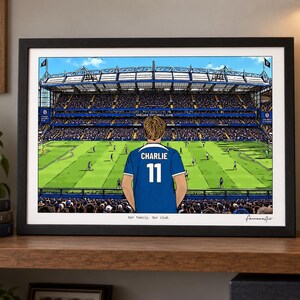 Puede incluir: Una impresi&oacute;n art&iacute;stica horizontal enmarcada que representa un estadio de f&uacute;tbol con una persona vistiendo una camiseta azul con el nombre CHARLIE y el n&uacute;mero 11 en la espalda. El texto Our family. Our club. aparece en la parte inferior central.