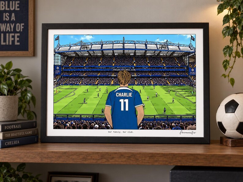 Puede incluir: Una impresi&oacute;n art&iacute;stica horizontal enmarcada que representa un estadio de f&uacute;tbol con una persona vistiendo una camiseta azul con el nombre CHARLIE y el n&uacute;mero 11 en la espalda. El texto Our family. Our club. aparece en la parte inferior central.