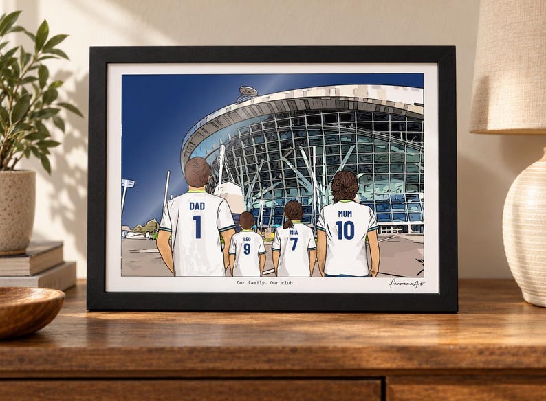 Puede incluir: Una ilustraci&oacute;n enmarcada de cuatro personas vistas desde atr&aacute;s con camisetas de f&uacute;tbol blancas con n&uacute;meros y nombres en azul, frente a un gran estadio. Las camisetas dicen DAD 1, LEO 9, MIA 7 y MUM 10. El texto Our family. Our club. aparece impreso debajo.