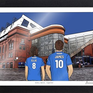 May include: A framed digital illustration of two individuals wearing blue soccer jerseys with the names ELLIE and JAMES and numbers 8 and 10 on the back, standing before a large red brick stadium. The text Every match, together is printed below.