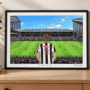 May include: A framed art print depicting a soccer stadium view from the stands. A person stands in the foreground wearing a black and white striped jersey with the name CHARLIE and the number 11 on the back. Text reads Our family. Our club.