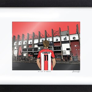 May include: A framed illustration of a person wearing a red and white striped jersey with the name CHARLIE and number 11 on the back, standing before a stadium with the text The Blade visible on the structure and Our club. Our memories. below.