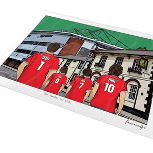 Pu&ograve; includere: Una stampa con illustrazione digitale che mostra quattro persone viste di spalle che indossano maglie da calcio rosse con nomi e numeri. Le maglie riportano DAD 1, LEO 9, MIA 7 e MUM 10. Lo sfondo mostra uno stadio e il testo Our family. Our club.