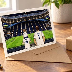 May include: A greeting card featuring an illustration of three people in white soccer jerseys with the numbers 1, 7, and 10, and the names DAD, IVY, and MUM on their backs, standing in a stadium. The text Happy Birthday, Dad is printed below.