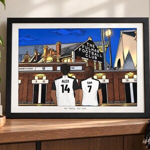 May include: A framed illustration of two people wearing white and black soccer jerseys with the names ALEX and SAM and numbers 14 and 7 on the back, standing before The Fulham Football Club stadium at night with the text Our family. Our club.