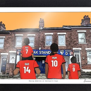 May include: A framed illustration of a family wearing red soccer jerseys with names and numbers on the back, standing before a brick building. The jerseys read Max 7, Dad 14, Mum 10, and Ava 9. The text below reads Making memories at Kenilworth Road.