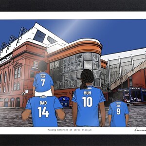May include: A framed digital illustration of four individuals wearing blue soccer jerseys with names and numbers on the back, standing before Ibrox Stadium. The text "Making memories at Ibrox Stadium" is printed at the bottom center of the print.