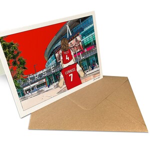 May include: A red and white illustrated greeting card featuring a cartoon of a person wearing a red and white soccer jersey with the number 7 on the back. The jersey has the name "Lunniss" on the back. The person is standing in front of a large stadium with the word "Arsenal" on the side. The background is red.