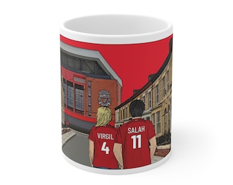 May include: White ceramic mug with a red, white, and gray illustration of two people wearing red soccer jerseys with the names "Virgil 4" and "Salah 11" on the back. The illustration shows the people walking down a street with a red brick building in the background.