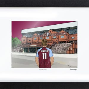 May include: A framed illustration of a person seen from behind, wearing a claret and blue soccer jersey with the name CHARLIE and number 11 printed on the back, standing before the Aston Villa stadium. The text Up the Villa! is printed below.