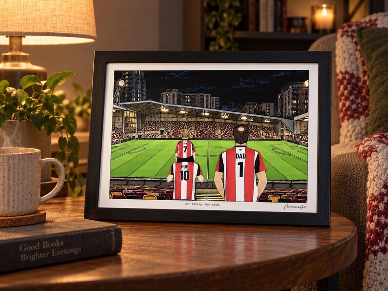 May include: A framed illustration of a family at a football stadium. The artwork depicts three people wearing red and white striped jerseys with the text MUM 10, DAD 1, and a child with 7. The text Our family: Our club is printed at the bottom.