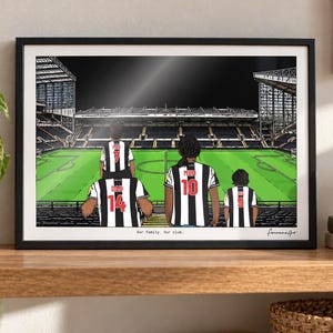 May include: A framed illustration of a family of four wearing black and white striped soccer jerseys with red numbers and names on the back, standing in a stadium. The text "Our family. Our club." is printed at the bottom of the artwork.