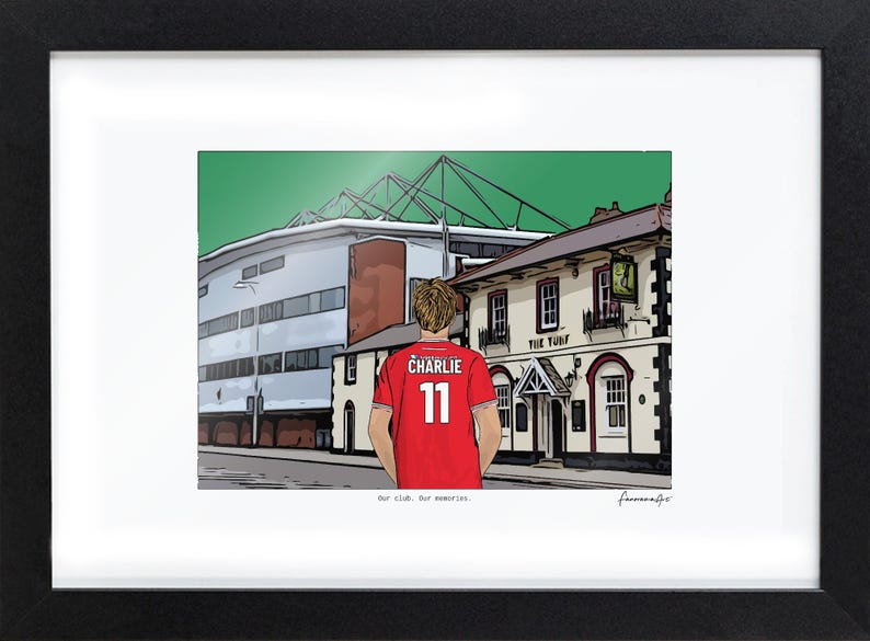Pu&ograve; includere: Un'illustrazione incorniciata che mostra una persona con una maglia rossa con il nome CHARLIE e il numero 11 sul retro, davanti a uno stadio e a un edificio con l'insegna THE TURF. Il testo Our club. Our memories. &egrave; stampato sotto.