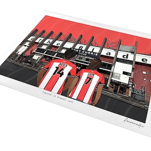 May include: A rectangular art print featuring a cartoon illustration of two people in red and white striped football shirts with the names ALEX 14 and SAM 7, standing before the Tony Currie Stand at Bramall Lane, with the text Together at Bramall Lane.