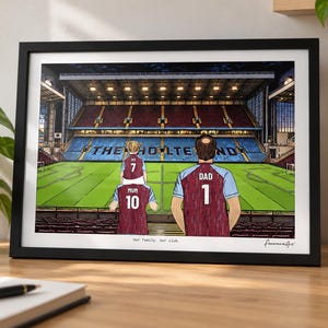 May include: A framed illustration of a soccer stadium interior with the text THE HOLTE END visible on the seating. Three figures in claret and blue jerseys stand in the foreground, with the text Our family. Our club. printed below the image.