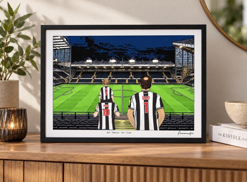 May include: A framed illustration of a soccer stadium with three people in black and white striped jerseys standing in the stands. The jerseys feature the text DAD, MUM, and numbers 1, 10, and 7. The text Our Family. Our club. is printed below.
