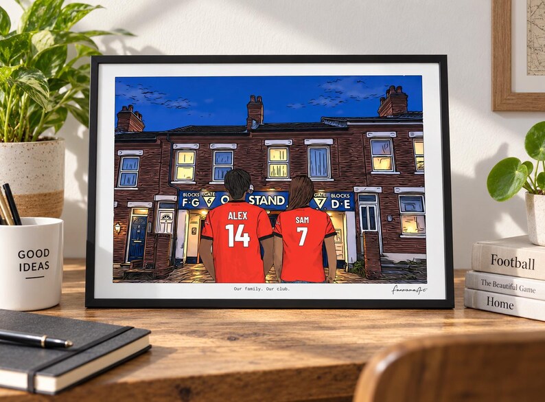 May include: A framed art print depicting two individuals wearing red soccer jerseys with the names Alex and Sam and numbers 14 and 7 on the back. They stand before a brick building with a blue sign reading Blocks Gate F G O Stand 7 D E.