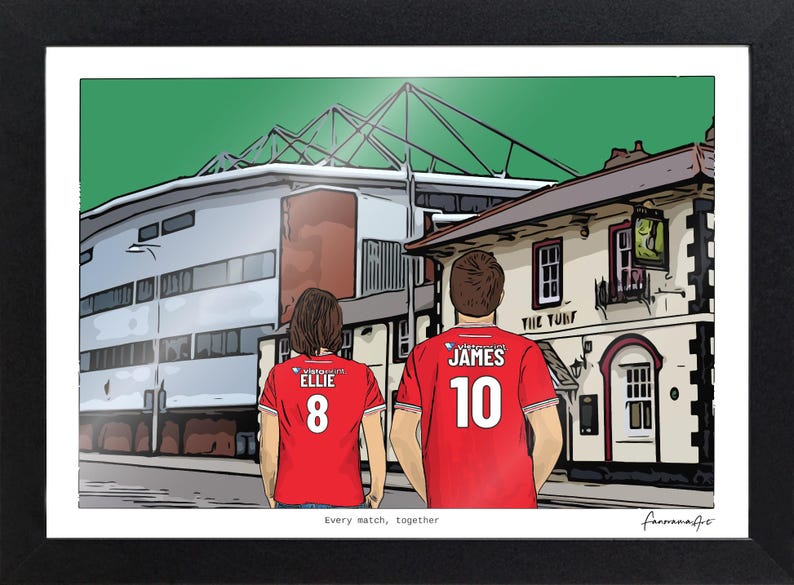 Pu&ograve; includere: Un'illustrazione digitale incorniciata mostra due figure viste di spalle che indossano maglie da calcio rosse con i nomi ELLIE e JAMES e i numeri 8 e 10 stampati sul retro. Lo sfondo presenta uno stadio e un edificio chiamato THE TURF.