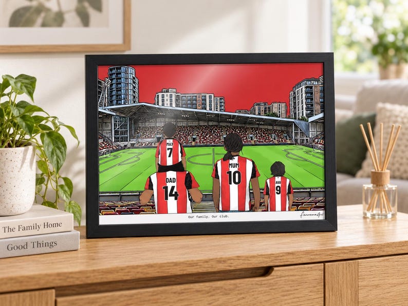 May include: A framed illustration of a family of four wearing red and white striped football shirts inside a stadium. The shirts feature the names Max, Dad, Mum, and Ava with numbers 7, 14, 10, and 9. The text "Our family. Our club." is printed below.