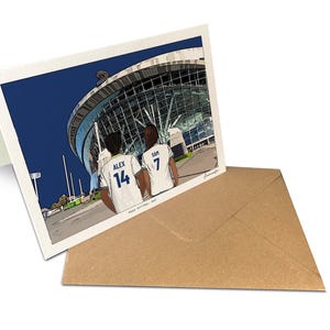 May include: A folded greeting card featuring a colorful illustration of two people in white sports jerseys with the names ALEX 14 and SAM 7 on the back, standing before a large stadium. The text Happy Birthday Sam is printed at the bottom.