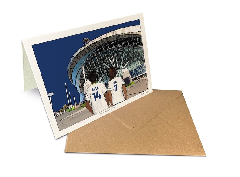 May include: A folded greeting card featuring a colorful illustration of two people in white sports jerseys with the names ALEX 14 and SAM 7 on the back, standing before a large stadium. The text Happy Birthday Sam is printed at the bottom.