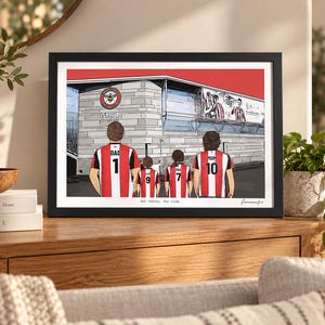 May include: A framed illustration of four people standing in front of a stadium, wearing red and white striped jerseys with numbers and names on the back. The text "Our family. Our club." is printed below the figures in a black frame.