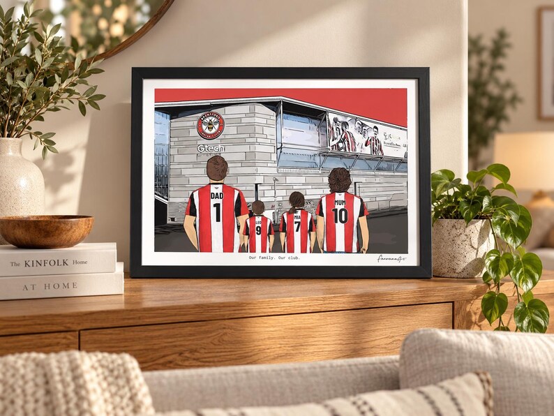 May include: A framed illustration of four people standing in front of a stadium, wearing red and white striped jerseys with numbers and names on the back. The text "Our family. Our club." is printed below the figures in a black frame.