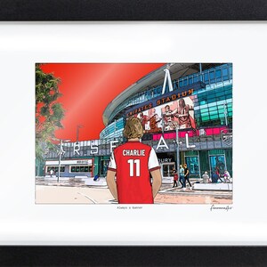 Bordered A4 Arsenal print in a black frame, showing Charlie 11 facing the Emirates Stadium. The smaller artwork leaves a white border on the printed sheet.