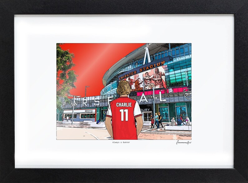 Bordered A4 Arsenal print in a black frame, showing Charlie 11 facing the Emirates Stadium. The smaller artwork leaves a white border on the printed sheet.