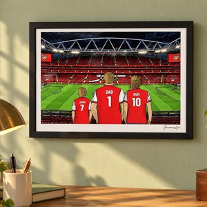 AI-created lifestyle mockup of a black framed A4 Arsenal print on a sage study wall above a desk and brass lamp, featuring Jamie 7, Dad 1 and Mum 10 with the Pitch Side at Night background.