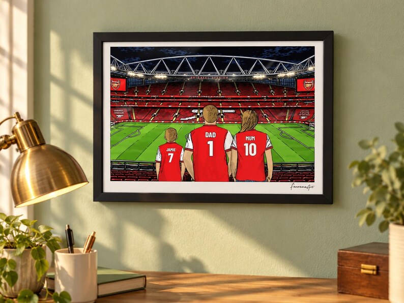 AI-created lifestyle mockup of a black framed A4 Arsenal print on a sage study wall above a desk and brass lamp, featuring Jamie 7, Dad 1 and Mum 10 with the Pitch Side at Night background.