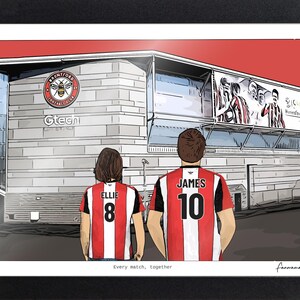 May include: A framed illustration of two individuals wearing red and white striped football shirts with the names Ellie and James and numbers 8 and 10 on the back. They stand before the Gtech Community Stadium with the Brentford FC logo visible.