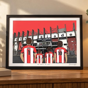 May include: A framed illustration of a family of four standing before the Tony Currie Stand at Bramall Lane. The figures wear red and white striped soccer jerseys with names and numbers on the back. The text reads Our family. Our club.
