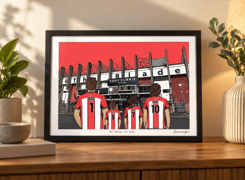 May include: A framed illustration of a family of four standing before the Tony Currie Stand at Bramall Lane. The figures wear red and white striped soccer jerseys with names and numbers on the back. The text reads Our family. Our club.