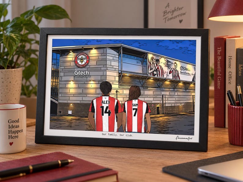 May include: A framed illustration of the Gtech Community Stadium featuring two people from behind wearing red and white striped football shirts with the names ALEX 14 and SAM 7. The text reads Gtech Community Stadium and Our family. Our club.