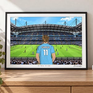 May include: A framed illustration of a soccer stadium featuring a person wearing a light blue jersey with the name CHARLIE and the number 11 on the back. The text Our family. Our club. is printed at the bottom center of the artwork.