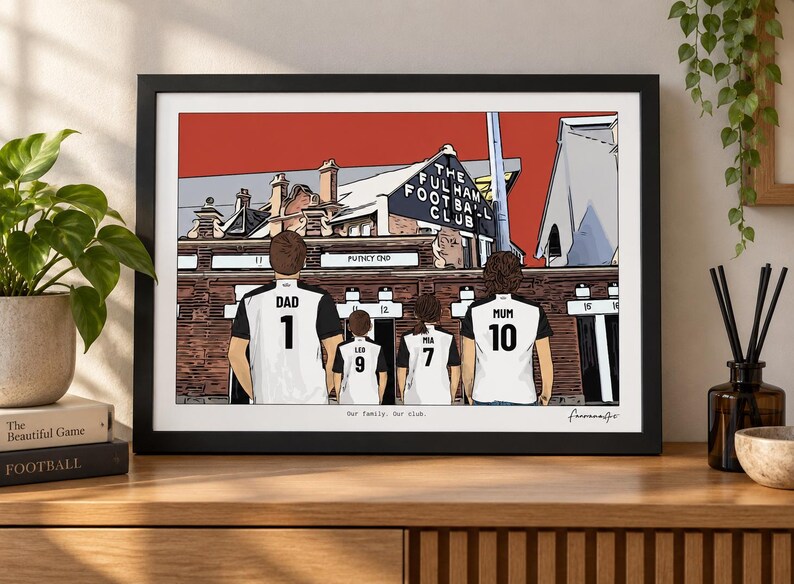 May include: A framed illustration of a family of four wearing white and black soccer jerseys with names and numbers, standing before the Fulham Football Club stadium. The text reads The Fulham Football Club, Our family. Our club.