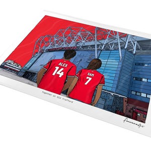 May include: A digital illustration print featuring two figures in red soccer jerseys with the names ALEX 14 and SAM 7, standing before the Old Trafford stadium. The text Together at Old Trafford is printed below the figures on a white background.