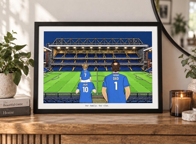 May include: A framed illustration of a soccer stadium with three people in blue jerseys standing in the foreground. The jerseys are labeled Mum 10, Dad 1, and a child with 7. The text Our family. Our club. is printed at the bottom of the print.